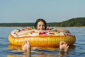 schattig tiener meisje met kleurrijk opblaasbaar zwemmen cirkel zwemt in de blauw water van de zee Aan een heet zonnig dag foto
