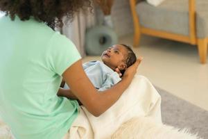 jong moeder Afrikaanse Amerikaans Holding haar een maand oud pasgeboren baby zoon voorzichtig en voorzichtig in slaapkamer. aanbiddelijk weinig zuigeling slaap goed in warm omhelzing van moederschap. gelukkig moeder dag concept foto