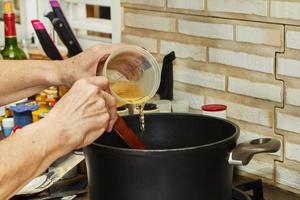 chef giet vloeistof in de Koken pot in de keuken Aan gas- fornuis foto