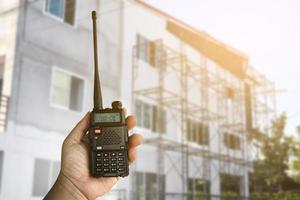 een portable radio zender Holding in hand, wazig een buitenshuis gebouw welke is bouwen, zacht en selectief focus. foto