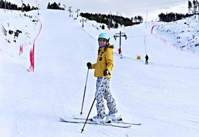 gelukkig glimlachen jong vrouw in geel jasje en ski helm skiën Aan een berg helling, winter sport, alpine skiën buitenshuis werkzaamheid, gezond levensstijl foto