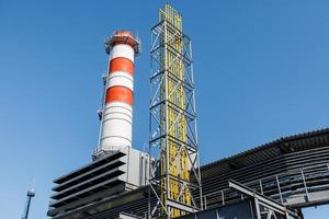 gas- turbine macht fabriek Aan natuurlijk gas- met schoorstenen van rood Wit kleur tegen een blauw lucht Aan een zonnig dag foto