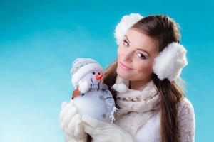 vrouw in warme kleren sneeuwpop speelgoed te houden. foto