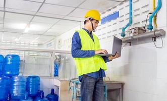 ingenieur werken in drinken water fabriek gebruik makend van een tablet computer naar controleren en reparatie boiler water naar de water systeem in fabriek foto