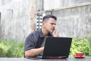aantrekkelijk jong Aziatisch Mens gebruik makend van laptop verward in samenwerken ruimte met ongelukkig gezicht foto