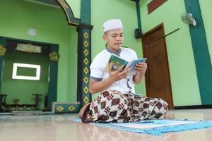 jong Aziatisch moslim bidden in de moskee en lezing al koran foto