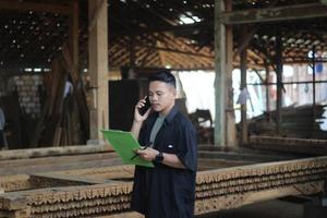 Aziatisch jong Mens baas van hout bedrijf roeping haar vriend en controle kwaliteit foto