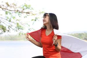 mooi jong Aziatisch vrouw draag- de Indonesisch vlag met een vrolijk gezicht foto