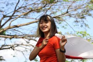 mooi jong Aziatisch vrouw draag- de Indonesisch vlag met een vrolijk gezicht foto