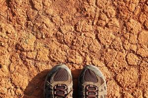 de poten van een Mens in sportschoenen een droog vervuild rood steenachtig bodem, top visie. foto