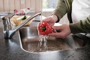 Mannen handen wassen klok paprika's onder rennen water, in een wasbak. nuttig vers paprika in de keuken. foto