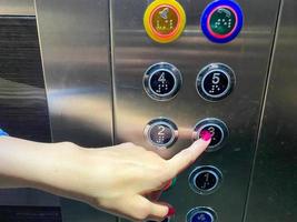 een vrouw gemanicuurd vinger Aan haar hand- persen een knop in een modern mooi lift in een hoogbouw gebouw foto