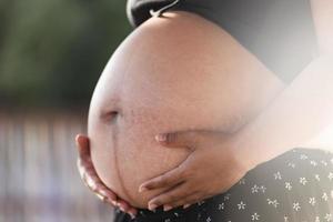 een detailopname schot van de buik van een 30 weken zwanger vrouw vervelend een zwart bodycon jurk. gaan Aan moederschap vertrekken, planning zwangerschap, voorbereidingen treffen voor bevalling foto