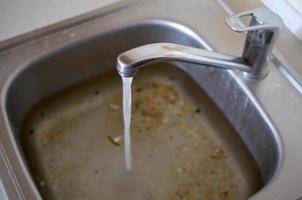 roestvrij staal wastafel plug gat dichtbij omhoog vol van water en deeltjes van voedsel foto