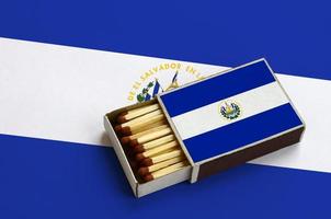 el Salvador vlag is getoond in een Open luciferdoosje, welke is gevulde met wedstrijden en leugens Aan een groot vlag foto