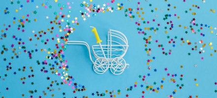 een jaar verjaardag.baby wandelwagen met kaars in het formulier van aantal een Aan blauw achtergrond met sterren confetti pailletten. banier foto