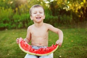 gelukkig glimlachen kind jongen aan het eten de watermeloen buitenshuis in de achtertuin foto