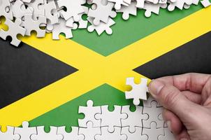 Jamaica vlag is afgebeeld Aan een tafel Aan welke de menselijk hand- vouwen een puzzel van wit kleur foto