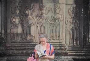 siem oogsten, Cambodja - oktober 04 2016 - Europese toerist lezing een gids boek in de Oppervlakte van Angkor wat met een apsara decoratie Bij bovenstaande. foto