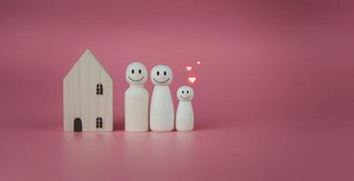 gelukkig huis concept. model- huis met houten poppen staand bekleed omhoog Aan roze achtergrond en hart pictogrammen. geeft aan geluk en liefde in de huis. foto