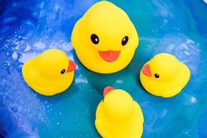mooi geel rubber bad speelgoed- eenden zwemmen Aan een blauw water achtergrond foto