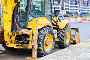 groot helder geel krachtig industrieel zwaar graafmachine tractor, bulldozer, gespecialiseerd bouw uitrusting voor weg reparatie gedurende de bouw van een nieuw micro-district in een groot stad foto