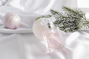 een elegant fles van vrouwen parfum leunde tegen een wit Kerstmis bal. wit satijn achtergrond met een Afdeling van sparren. feestelijk samenstelling. foto