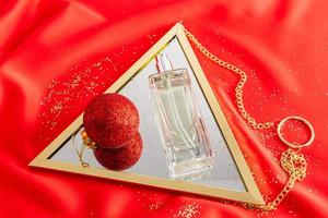 een glas fles van vrouwen parfum leugens Aan een spiegel met een rood Kerstmis bal. satijn rood achtergrond is de traditioneel kleur van de nieuw jaar. top visie. foto