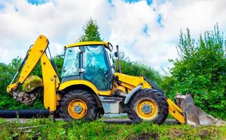 geparkeerd groot geel multifunctioneel wiel trekker Aan de glade tegen groen bomen in zonnig dag. geel backhoe foto