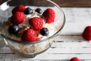 frambozen, bosbessen, granen en yoghurt in een glas kom Aan houten latten. gezond ontbijt voor een gezond leven. horizontaal afbeelding. foto