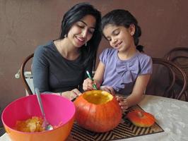 moeder en dochter die pret hebben tijdens het snijden van een halloween-pompoen foto