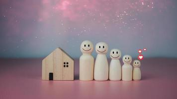 gelukkig huis concept. model- huis met houten poppen staand bekleed omhoog Aan roze achtergrond en hart pictogrammen. geeft aan geluk en liefde in de huis. foto