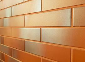 modern facade gemaakt van oranje keramisch tegels. nieuw muur betegeld helder oranje bakstenen met een zilverachtig grijs schaduw, schijnend in de zon. horizontaal perspectief terugwijkend in de afstand. achtergrond kopiëren ruimte. foto