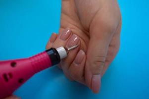de werkwijze van maken een mooi manicure Aan de vingers van een vinger verwerken een nagel met een speciaal machine in een nagel schoonheid salon Aan een blauw achtergrond foto
