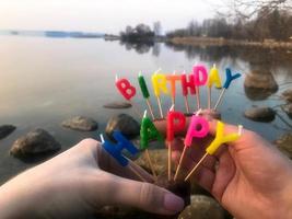 gelukkig verjaardag opschrift gemaakt van vakantie kaarsen in de handen van een Mens en een vrouw tegenover de water van de oceaan meer rivier- foto