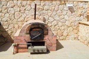 een groot professioneel industrieel bruin steen oven rooster oven met een buis voor Koken frituren voedsel van een steen betegeld Aan een steen muur achtergrond in de Open lucht straat foto