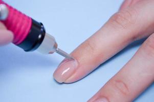 de werkwijze van maken een mooi manicure Aan de vingers van een vinger verwerken een nagel met een speciaal machine in een nagel schoonheid salon Aan een blauw achtergrond foto