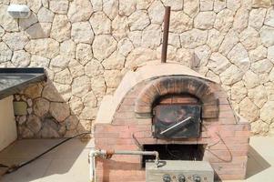 een groot professioneel industrieel bruin steen oven rooster oven met een buis voor Koken frituren voedsel van een steen betegeld Aan een steen muur achtergrond in de Open lucht straat foto