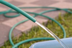 detailopname groen tuin slang was gegoten water van rubber buis zetten in de blauw emmer Bij tuin. foto