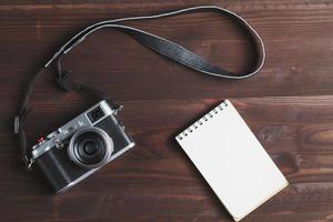 blanco kladblok bladzijde en modern camera in klassiek stijl Aan donker bruin houten tafel foto