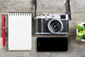 klassiek camera met blanco kladblok bladzijde en rood pen Aan grijs houten, wijnoogst bureau met telefoon. foto