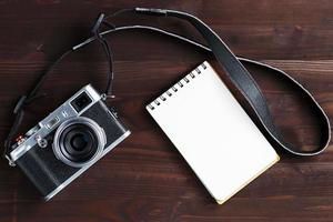 blanco kladblok bladzijde en modern camera in klassiek stijl Aan donker bruin houten tafel foto