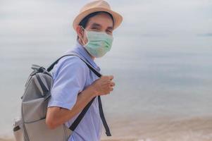 Mens slijtage gezicht masker Holding zak reizen Aan strand foto