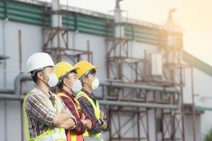 groep van drie jong ingenieurs arbeider veiligheid hesje en helm, kijken Bij dezelfde manier naar de industrieel fabriek achtergrond foto