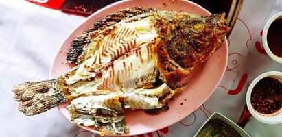 top visie van Thais gegrild tilapia, karper of granaatappel vis Aan roze bord of schotel met pittig en zoet saus Bij lokaal straat voedsel restaurant. gezond aan het eten en eetpatroon voedsel. foto