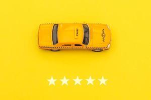 gele speelgoedauto taxicabine en 5 sterren rating geïsoleerd op gele achtergrond. smartphone-applicatie van taxiservice voor online zoeken, bellen en boeken van cabineconcept. taxi-symbool. ruimte kopiëren. foto