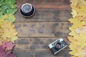 een kop van thee en een oud camera tussen een reeks van vergeling gedaald herfst bladeren Aan een achtergrond oppervlakte van natuurlijk houten borden van donker bruin kleur foto