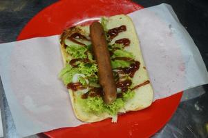 Indonesië lokaal hotdog. gebraden rundvlees, worst, sesam brood, sla, mayonaise en saus. hotdog maken werkwijze. straat voedsel. foto