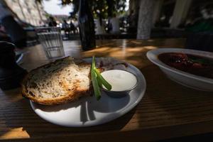 dichtbij omhoog visie plakjes van gerookt spek vlees met rogge geheel graan zwart brood, groen ui en verzuren room Aan de tafel. foto