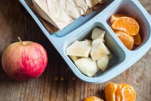 schooljongen lunch doos Aan houten achtergrond.appel,mandarijn,sandwich in lunchbox foto